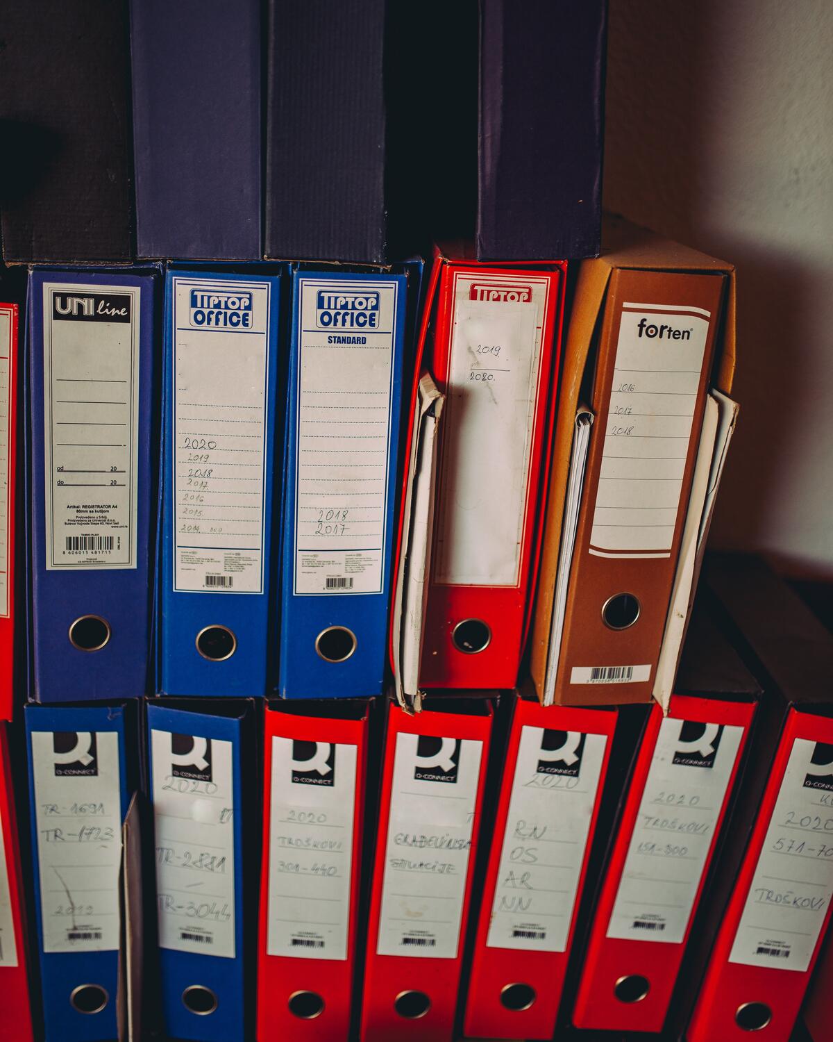 Een kast vol blauwe, rode en oranje ordners met etiketten op de rug