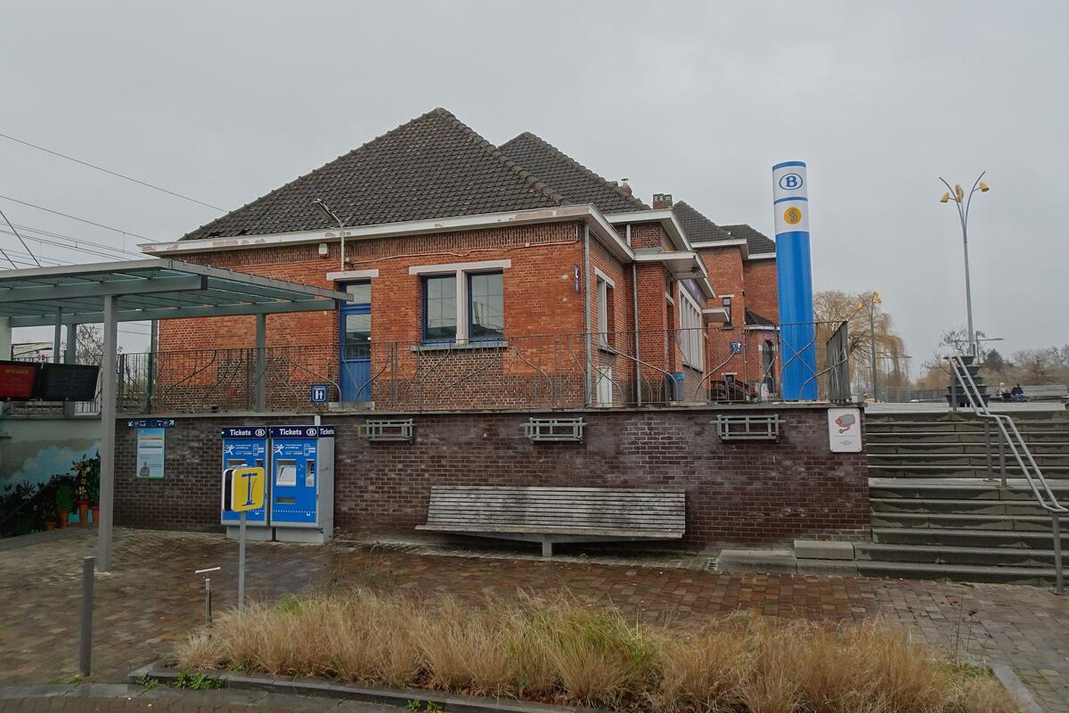 De ingang van station Duffel met een trap, een fietsenstalling en de blauwe paal van de spoorwegen