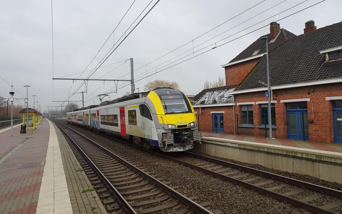 Een trein staat aan het perron van station Duffel, naast het bakstenen stationsgebouw met blauwe deuren